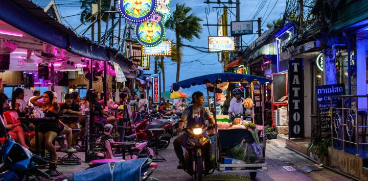Un vendedor ambulante de comida pasa en moto junto a bares cerca de la playa de Pattaya, en Pattaya, Tailandia.