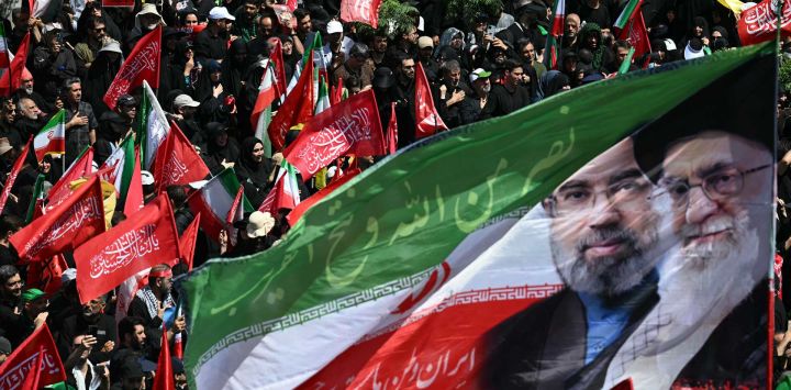 Los dolientes ondean una bandera con los retratos del actual líder supremo de Irán, Mojtaba Khamenei (izquierda), y su padre asesinado, Ali Khamenei, durante una procesión fúnebre en honor al líder supremo iraní asesinado, Ali Khamenei, y miembros de su familia en Teherán.