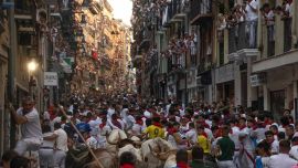 Los participantes corren delante de los toros de la ganadería Fuente Ymbro durante el primer encierro de las fiestas de San Fermín en Pamplona, norte de España. Miles de personas asisten cada año a las fiestas, que duran una semana, y a sus famosos encierros, en los que seis toros son liberados a las 8:00 de la mañana para correr desde su corral hasta la plaza de toros por las estrechas calles del casco antiguo, recorriendo una distancia de 850 metros. Los corredores que van delante intentan mantenerse cerca de los toros sin caerse ni ser corneados.