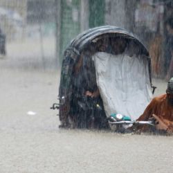 Un conductor de bicitaxi camina vadeando una calle inundada tras las fuertes lluvias en Chittagong, Bangladés. | Foto:AFP