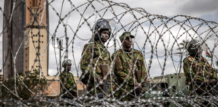 Agentes de la policía antidisturbios keniana montan guardia tras una barricada de alambre de púas mientras las autoridades imponen controles de carretera y el cierre parcial de las principales vías durante la marcha prevista de Saba Saba en el centro de Nairobi. La policía keniana prohibió la marcha, que conmemoraba un día anual de protesta, utilizando agentes de paisano y vehículos sin distintivos para dispersar incluso al pequeño grupo que logró reunirse.