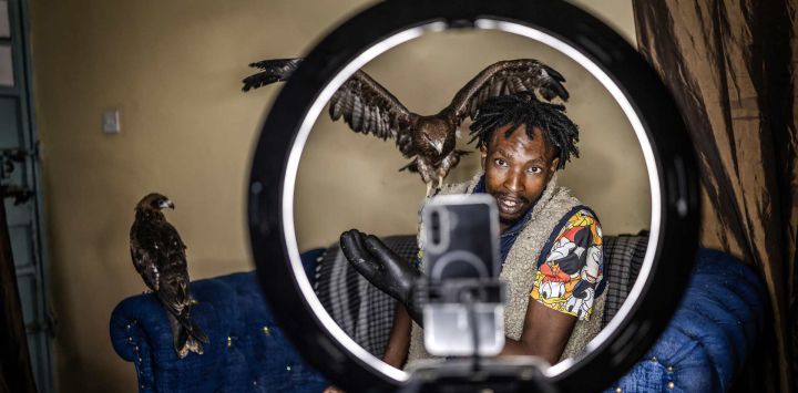 Rodgers Oloo Magutha, de 28 años, conocido popularmente como el "Hombre Pájaro de Nairobi", graba un video para sus redes sociales rodeado de algunas de las aves silvestres a su cargo mientras las alimenta en su apartamento de una habitación en Kayole, un barrio de bajos ingresos en las afueras de Nairobi. Tras haber sido un adolescente sin hogar que sobrevivía en las calles de Nairobi, Rodgers Oloo Magutha, se ha transformado en uno de los conservacionistas comunitarios más singulares de Kenia.