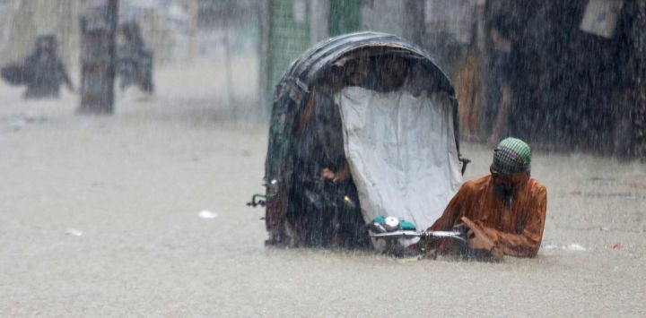 Un conductor de bicitaxi camina vadeando una calle inundada tras las fuertes lluvias en Chittagong, Bangladés.