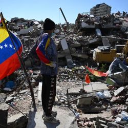 Un hombre se encuentra junto a una bandera venezolana mientras una retroexcavadora retira escombros en Caraballeda, estado de La Guaira, Venezuela, tras los terremotos que azotaron la región. | Foto:Raúl Arboleda / AFP