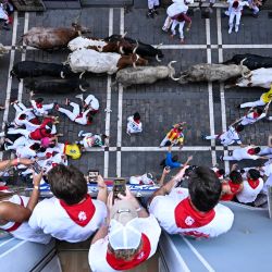 Varias personas observan desde un balcón cómo los participantes corren delante de los toros durante el primer encierro de las fiestas de San Fermín en Pamplona, al norte de España. | Foto:ANDER GILLENEA / AFP