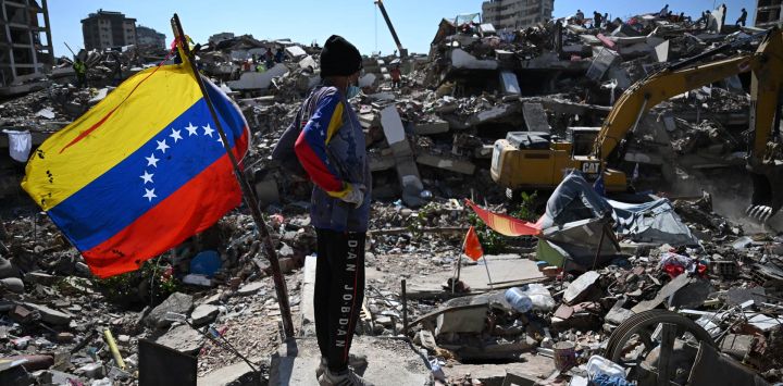 Un hombre se encuentra junto a una bandera venezolana mientras una retroexcavadora retira escombros en Caraballeda, estado de La Guaira, Venezuela, tras los terremotos que azotaron la región.