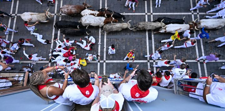 Varias personas observan desde un balcón cómo los participantes corren delante de los toros durante el primer encierro de las fiestas de San Fermín en Pamplona, al norte de España.