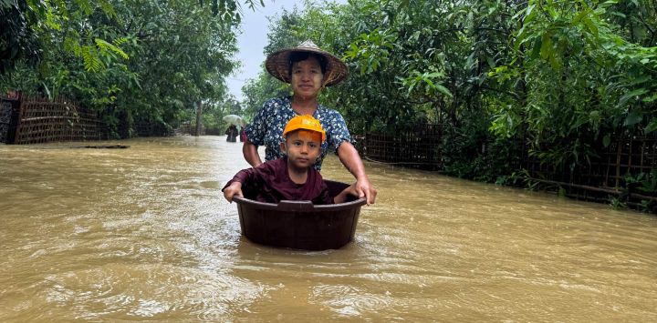 Un residente camina entre las aguas de la inundación con un niño en una bañera, que utilizaba un dispositivo de flotación, en Kyauktaw, estado de Rakhine, al oeste de Myanmar.