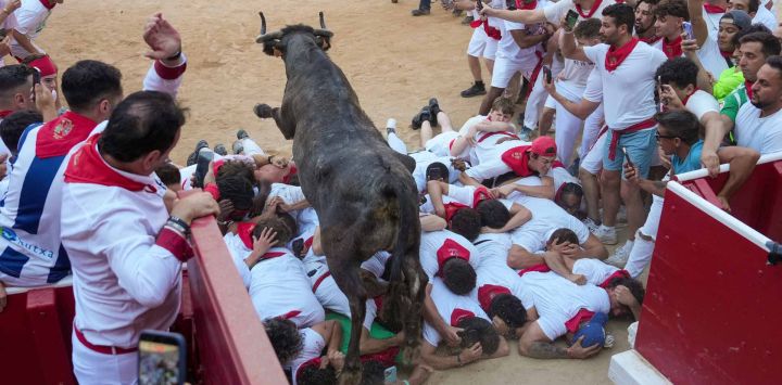 Una ternera salta por encima de los participantes en la plaza de toros mientras corren e intentan esquivarla tras el encierro de las fiestas de San Fermín en Pamplona, al norte de España.