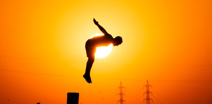 Un joven iraquí se zambulle desde un poste en el río Shatt al-Arab en Basora para refrescarse en medio de las altas temperaturas del verano, al atardecer.