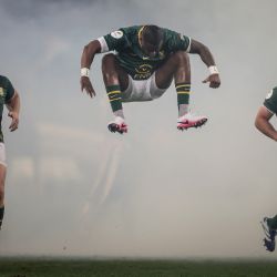 El zaguero sudafricano Aphelele Fassi salta al entrar al campo junto a los talonadores sudafricanos Jan-Hendrik Wessels y Andre-Hugo Venter durante el partido del Campeonato de Naciones de Rugby entre Sudáfrica y Gales en el estadio Kings Park de Durban. | Foto:Phill Magakoe / AFP