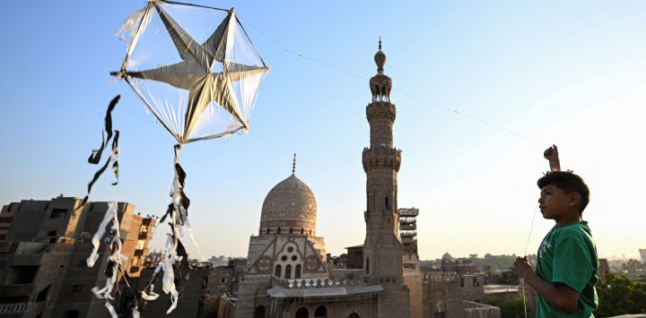 Un niño egipcio hace volar una cometa desde la azotea de su casa, frente al complejo funerario del sultán Qaytbay, durante la inauguración de la cúpula restaurada del mausoleo en El Cairo.