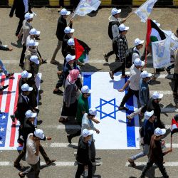 Estudiantes universitarios caminan sobre representaciones de las banderas de Estados Unidos, Israel y el Reino Unido mientras marchan en una manifestación para mostrar su apoyo al movimiento hutí en medio de la escalada de tensiones con Arabia Saudita, en el campus de la Universidad de Sanaa, en la capital de Yemen controlada por los hutíes. | Foto:MOHAMMED HUWAIS / AFP