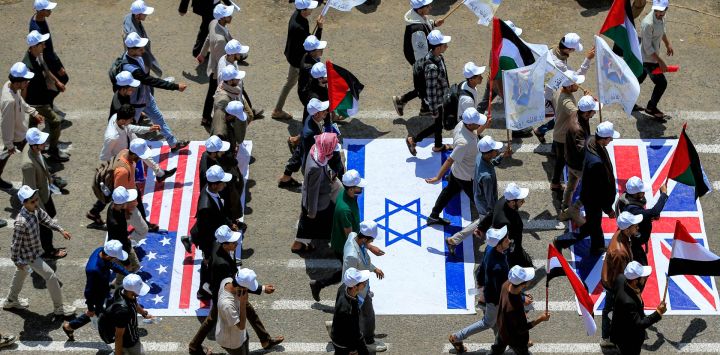 Estudiantes universitarios caminan sobre representaciones de las banderas de Estados Unidos, Israel y el Reino Unido mientras marchan en una manifestación para mostrar su apoyo al movimiento hutí en medio de la escalada de tensiones con Arabia Saudita, en el campus de la Universidad de Sanaa, en la capital de Yemen controlada por los hutíes.