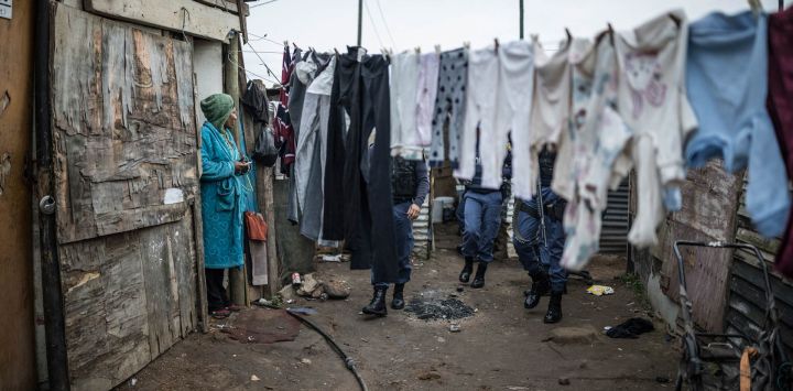 Una mujer observa cómo agentes del Servicio de Policía de Sudáfrica abandonan la vivienda de un residente sospechoso de albergar objetos robados en el municipio de Pellsrus, en Jeffreys Bay. La policía sudafricana informó que había arrestado a 69 personas tras una protesta antiinmigrante en la costa sureste del país que derivó en saqueos y dejó al menos una persona hospitalizada. Sudáfrica se ha visto sacudida durante semanas por protestas y disturbios contra inmigrantes indocumentados, lo que ha provocado que decenas de miles huyan del país.