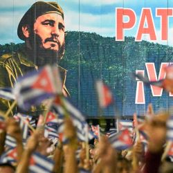 Cubanos ondean banderas de papel frente a una valla publicitaria con la imagen del fallecido líder Fidel Castro durante la celebración del 73.º aniversario del asalto guerrillero al Cuartel Moncada, liderado por Fidel Castro y considerado el inicio de la Revolución Cubana, en Pinar del Río, Cuba. Díaz-Canel denunció la "política genocida" de Washington hacia Cuba, acusando a Estados Unidos de intentar "apropiarse del país" mientras el presidente Donald Trump intensifica una estrategia de máxima presión contra la isla, junto con el embargo impuesto en 1962. | Foto:YAMIL LAGE / AFP