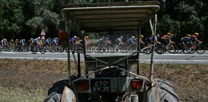 El pelotón de ciclistas pasa junto a un tractor al borde de la carretera durante la 18.ª etapa de la 113.ª edición del Tour de Francia, un recorrido de 185,2 km entre Voiron y Orcières-Merlette en los Alpes franceses.