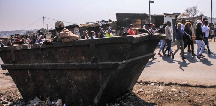 Un hombre se encuentra dentro de un contenedor de basura mientras miembros del movimiento March and March desfilan durante una manifestación semanal en Diepsloot, Johannesburgo, Sudáfrica.