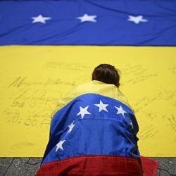 Un sindicalista envuelto en una bandera nacional venezolana, firma otra bandera nacional venezolana durante una marcha de protesta en demanda de elecciones en Caracas. | Foto:Federico Parra / AFP