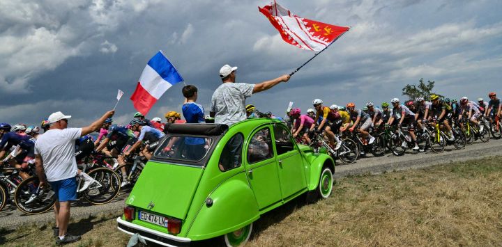 Espectadores a bordo de un Citroën 2CV ondean banderas mientras el pelotón ciclista pasa durante la 14.ª etapa de la 113.ª edición del Tour de Francia, un recorrido de 155,3 km entre Mulhouse y Le Markstein, en las montañas de los Vosgos.