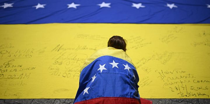 Un sindicalista envuelto en una bandera nacional venezolana, firma otra bandera nacional venezolana durante una marcha de protesta en demanda de elecciones en Caracas.
