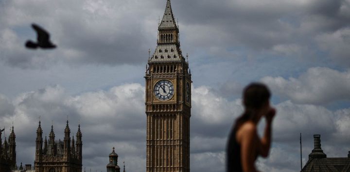 Una mujer se sienta en la orilla sur del río Támesis con vistas a la Torre Elizabeth (al fondo, en el centro), conocida popularmente como "Big Ben", y al Palacio de Westminster (abajo, a la izquierda), en la orilla norte, en Westminster, en el centro de Londres.