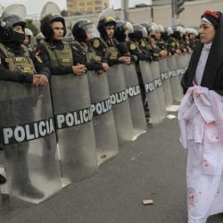 Una manifestante vestida de monja camina frente a agentes de policía durante una protesta de víctimas de crímenes presuntamente cometidos por el Estado peruano y contra la presidenta electa de Perú, Keiko Fujimori, frente al Palacio de Justicia en Lima. | Foto:Anthony Nino de Guzman / AFP