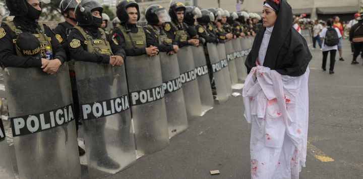 Una manifestante vestida de monja camina frente a agentes de policía durante una protesta de víctimas de crímenes presuntamente cometidos por el Estado peruano y contra la presidenta electa de Perú, Keiko Fujimori, frente al Palacio de Justicia en Lima.