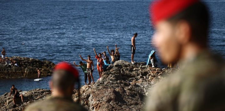 Miembros de las fuerzas de infantería regulares del Ejército español observan a un grupo de migrantes cerca del puesto fronterizo del enclave español de Ceuta. Al menos 72 personas murieron durante la llegada masiva de migrantes a Ceuta la semana pasada, cuando decenas de miles de personas, en su mayoría nadando, rodearon el puesto fronterizo desde Marruecos, según informaron hoy las autoridades locales. La mayoría de las aproximadamente 60.000 personas que se precipitaron al territorio español del norte de África han regresado a Marruecos tras el mayor cruce migratorio masivo en la historia del país.
