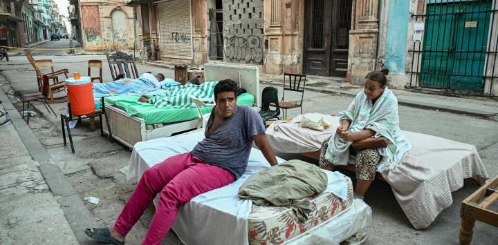 Residentes sentados y acostados en camas colocadas en una calle del barrio de Centro Habana tras el derrumbe parcial de su edificio en La Habana. Los cubanos se enorgullecen de afrontar las dificultades con resiliencia e ingenio, pero esa fortaleza está teniendo un alto costo psicológico en medio de la última crisis prolongada de la isla.