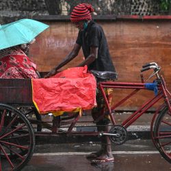 Un hombre cubre su triciclo con una lona de plástico en medio de la lluvia en Chennai, India. | Foto:R.Satish BABU / AFP