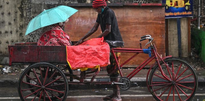 Un hombre cubre su triciclo con una lona de plástico en medio de la lluvia en Chennai, India.