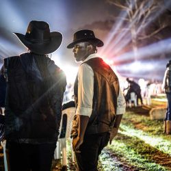 Durante las celebraciones del Día Internacional del Vaquero, en el hipódromo de Ngong en Nairobi, asistentes vestidos de vaquero observan desde la distancia una actuación de música country en directo. Celebrado anualmente el Día Internacional del Vaquero conmemora la historia, la cultura y el legado perdurable de los vaqueros y vaqueras de todo el mundo. Si bien tiene sus raíces en las tradiciones de Norteamérica, la cultura vaquera y la música country han ganado cada vez más adeptos en algunas partes de África en los últimos años, especialmente en Kenia, donde la moda del Oeste, el baile en línea, la equitación y los eventos de música country han atraído a una creciente comunidad de aficionados. | Foto:LUIS TATO / AFP