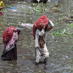 Personas que transportan sacos de verduras caminan con dificultad por un mercado inundado tras las fuertes lluvias en Lahore, Pakistán. | Foto:Arif Ali / AFP