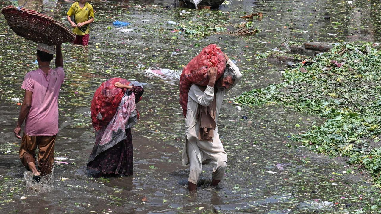 Personas que transportan sacos de verduras caminan con dificultad por un mercado inundado tras las fuertes lluvias en Lahore, Pakistán. | Foto:Arif Ali / AFP