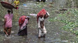 Personas que transportan sacos de verduras caminan con dificultad por un mercado inundado tras las fuertes lluvias en Lahore, Pakistán.