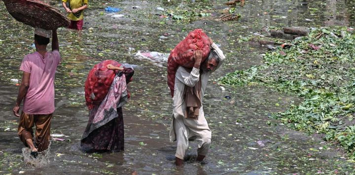 Personas que transportan sacos de verduras caminan con dificultad por un mercado inundado tras las fuertes lluvias en Lahore, Pakistán.