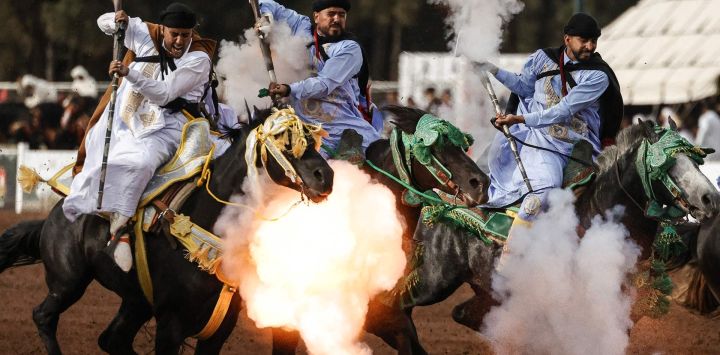 Jinetes marroquíes, ataviados con vestimenta tradicional, disparan fusiles durante una exhibición ecuestre de Fantasía, en el Trofeo Hassan II Tbourida, celebrado en Rabat. Esta disciplina ecuestre tradicional, consiste en cargas de caballería seguidas de salvas de fusil sincronizadas, preservando así un patrimonio cultural marroquí reconocido por la UNESCO como Patrimonio Cultural Inmaterial de la Humanidad.