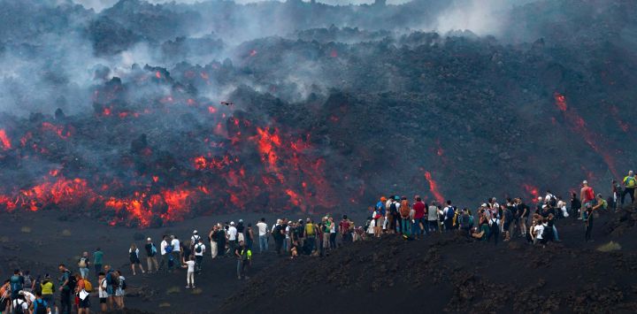 Esta fotografía, distribuida por Etna Walk, muestra a visitantes junto a la lava que fluye del volcán Etna durante una erupción en Catania, en la isla mediterránea de Sicilia, Italia.