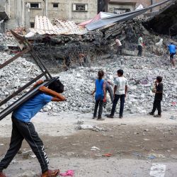 Un niño camina cargando una mesa a la espalda junto a trabajadores que desmantelan los escombros de un edificio destruido durante la guerra de Israel contra Hamás en Gaza, para reutilizar los restos en el futuro, en la ciudad de Gaza. | Foto:OMAR AL-QATTAA / AFP