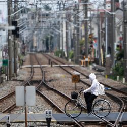 Una mujer se cubre para protegerse del sol mientras cruza en bicicleta las vías del tren en un día caluroso en Tokio, Japón. | Foto:ANDREW CABALLERO-REYNOLDS / AFP