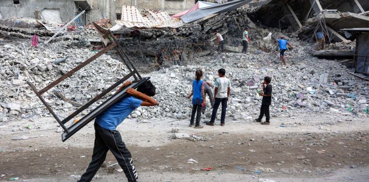 Un niño camina cargando una mesa a la espalda junto a trabajadores que desmantelan los escombros de un edificio destruido durante la guerra de Israel contra Hamás en Gaza, para reutilizar los restos en el futuro, en la ciudad de Gaza.