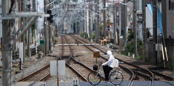 Una mujer se cubre para protegerse del sol mientras cruza en bicicleta las vías del tren en un día caluroso en Tokio, Japón.