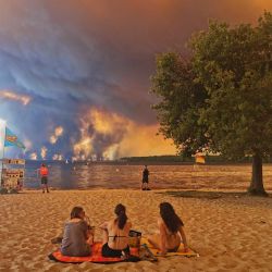 Bañistas se sientan en la playa de Moutchic, en Lacanau, al suroeste de Francia, mientras columnas de humo se elevan hacia el cielo a causa de un incendio forestal. El fuego, que azota la zona norte de la cuenca de Arcachon, en la región de Gironda, al suroeste de Francia, ha arrasado más de 3.400 hectáreas, según las últimas cifras publicadas por la prefectura. | Foto:Maximilien Lamy / AFP