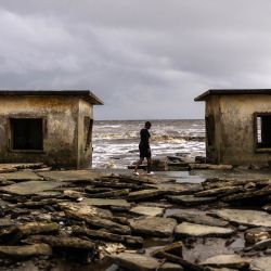 Un residente camina entre los edificios del Palacio Real dañados por la erosión costera en Ayetoro, estado de Ondo. La comunidad costera de Ayetoro, en el estado de Ondo, al suroeste de Nigeria, se ha convertido en uno de los ejemplos más visibles del país sobre la vulnerabilidad de las comunidades que viven a lo largo del océano Atlántico ante la erosión costera y el aumento del nivel del mar. Desde principios de la década de 2000, la erosión costera en Ayetoro se ha intensificado progresivamente, con el océano Atlántico invadiendo gradualmente el asentamiento, engullendo casas, escuelas y otras infraestructuras, y obligando a algunos residentes a reubicarse varias veces. | Foto:OLYMPIA DE MAISMONT / AFP