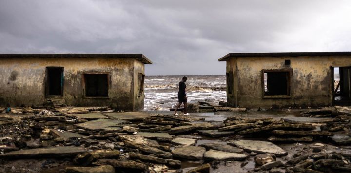 Un residente camina entre los edificios del Palacio Real dañados por la erosión costera en Ayetoro, estado de Ondo. La comunidad costera de Ayetoro, en el estado de Ondo, al suroeste de Nigeria, se ha convertido en uno de los ejemplos más visibles del país sobre la vulnerabilidad de las comunidades que viven a lo largo del océano Atlántico ante la erosión costera y el aumento del nivel del mar. Desde principios de la década de 2000, la erosión costera en Ayetoro se ha intensificado progresivamente, con el océano Atlántico invadiendo gradualmente el asentamiento, engullendo casas, escuelas y otras infraestructuras, y obligando a algunos residentes a reubicarse varias veces.