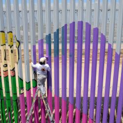 Esta vista aérea muestra a la voluntaria Joselyn Valladares pintando el muro fronterizo entre Estados Unidos y México en homenaje a las madres de personas desaparecidas, como parte de una campaña de Amnistía Internacional para crear conciencia sobre las personas desaparecidas y las familias que las buscan, en Playas de Tijuana, Baja California, México. | Foto:Guillermo Arias / AFP