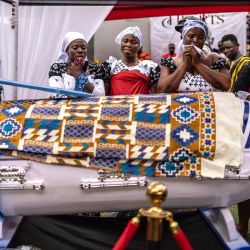 Familiares lloran junto al ataúd con forma de pluma del difunto profesor ghanés Samuel Commey Tetteh durante su funeral en Paanor, Ghana. Los ataúdes con formas especiales son una tradición funeraria ghanesa distintiva, particularmente asociada con el pueblo Ga de la región del Gran Accra. Conocidos localmente como abebuu adekai ("cajas de proverbios"), se elaboran artesanalmente con la forma de objetos, animales o vehículos que reflejan la profesión, la personalidad o los intereses del difunto, desde un pez para un pescador hasta un zapato para un futbolista. | Foto:OLYMPIA DE MAISMONT / AFP