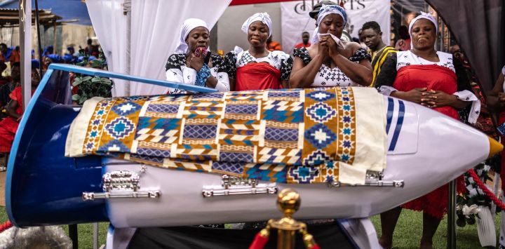 Familiares lloran junto al ataúd con forma de pluma del difunto profesor ghanés Samuel Commey Tetteh durante su funeral en Paanor, Ghana. Los ataúdes con formas especiales son una tradición funeraria ghanesa distintiva, particularmente asociada con el pueblo Ga de la región del Gran Accra. Conocidos localmente como abebuu adekai ("cajas de proverbios"), se elaboran artesanalmente con la forma de objetos, animales o vehículos que reflejan la profesión, la personalidad o los intereses del difunto, desde un pez para un pescador hasta un zapato para un futbolista.