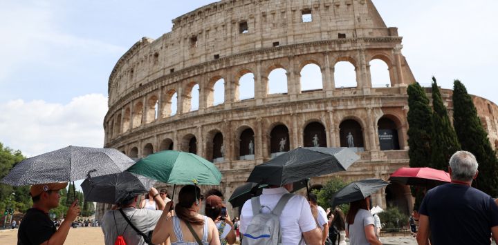 Turistas se protegen del Sol con sombrillas cerca del Coliseo durante una ola de calor, en Roma, Italia.